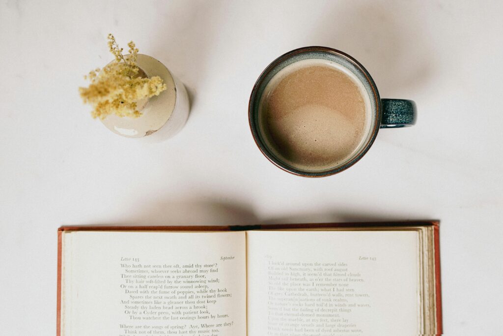 A serene scene featuring a ceramic mug of coffee, an open poetry book, and a vase with dried flowers.